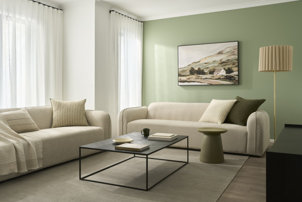 Living room of the Winton 25 display home at Lucas Estate Ballarat featuring neutral modern interiors, sage green feature wall, curved sofas, sheer curtains and contemporary styling