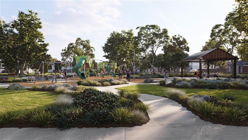 A modern community park featuring a children’s playground with green slides and swings, surrounded by lush lawns, trees, garden beds, and a covered picnic area.