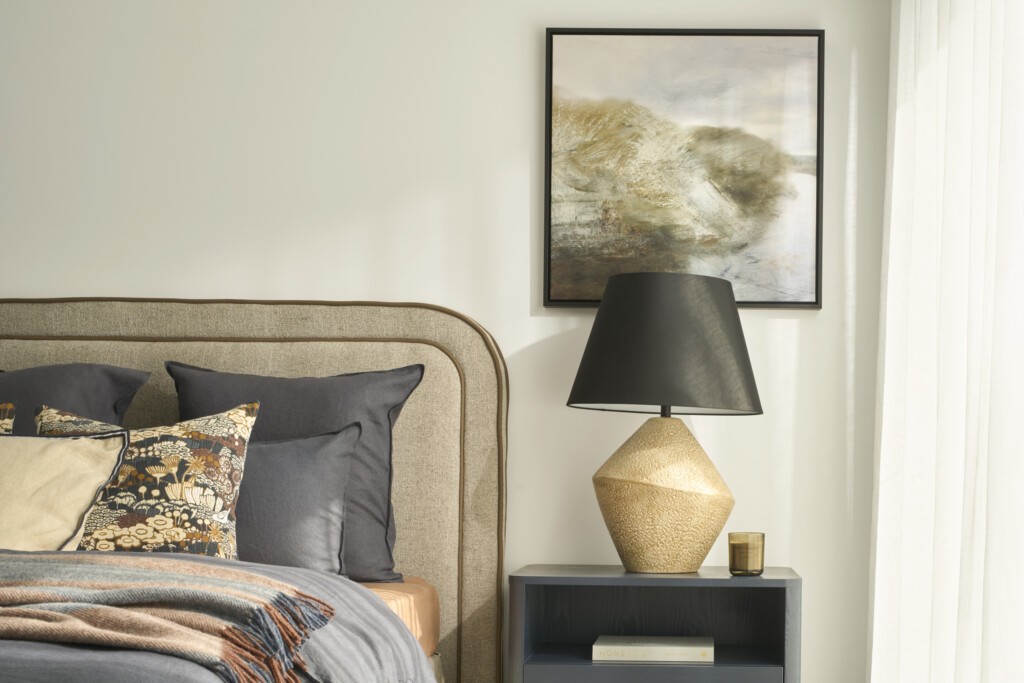 Stylish bedroom detail in the Hunter 26 at Riverfield Estate featuring a textured upholstered bedhead, layered cushions, bedside table with sculptural lamp and soft natural light.