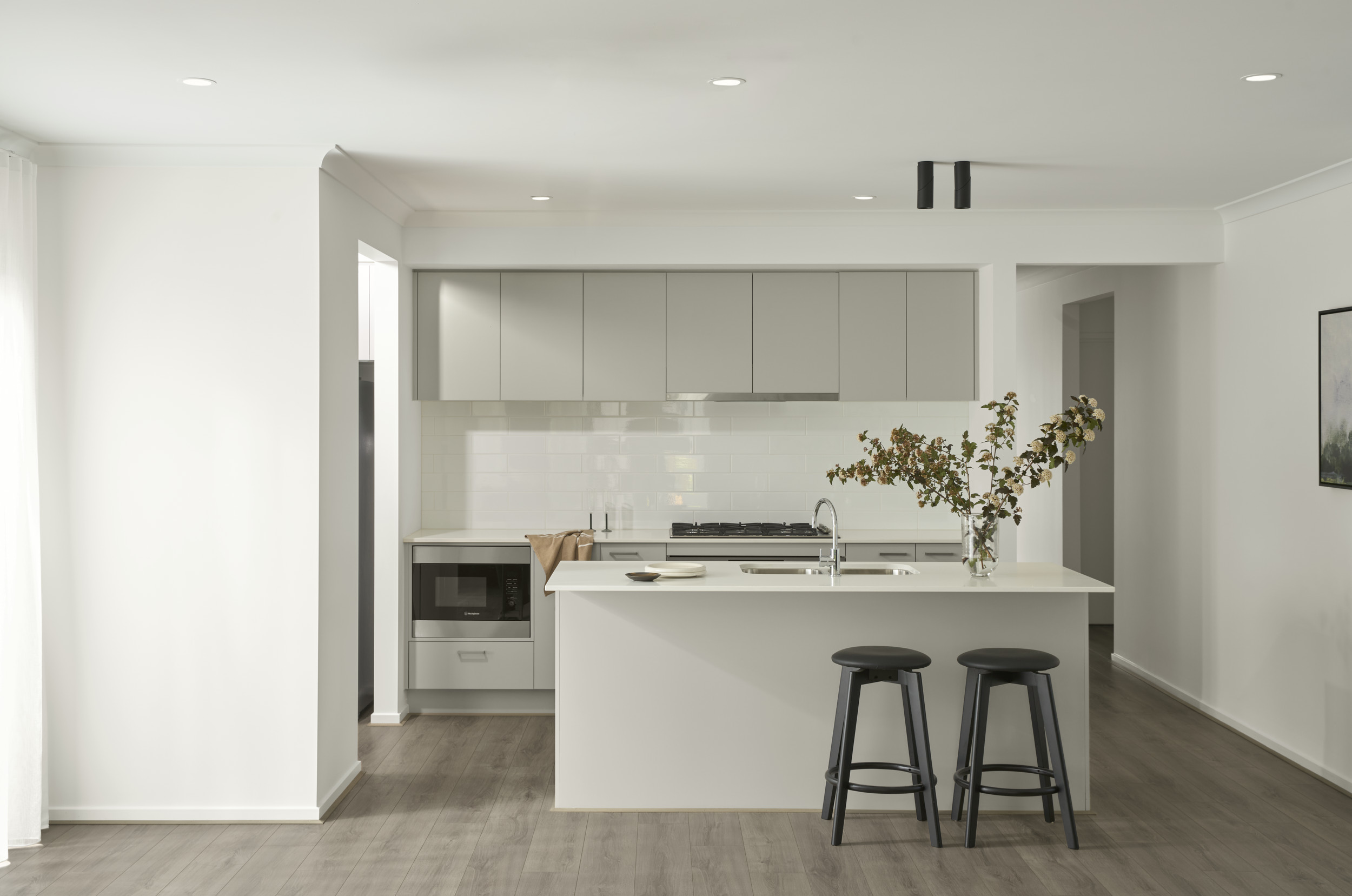 Modern kitchen in the Hunter 26 at Riverfield Estate featuring a large island bench, light cabinetry, subway tile splashback, stainless steel appliances and timber-look flooring.