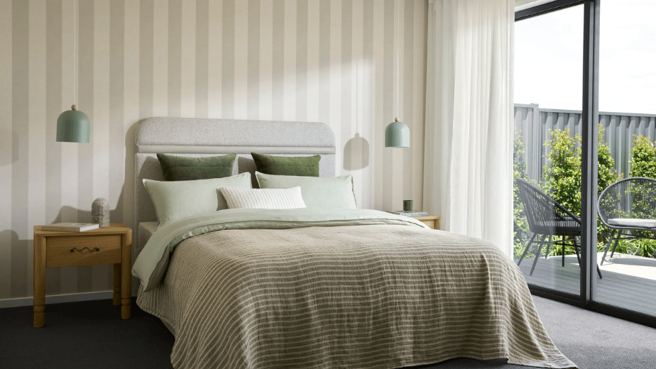 Master bedroom in the Winton 25 display home at Lucas Estate Ballarat featuring striped wallpaper, sage green bedding, pendant bedside lights and access to an outdoor patio.